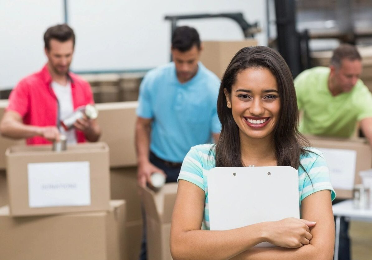 A girl smiling on front and three man putting food on box